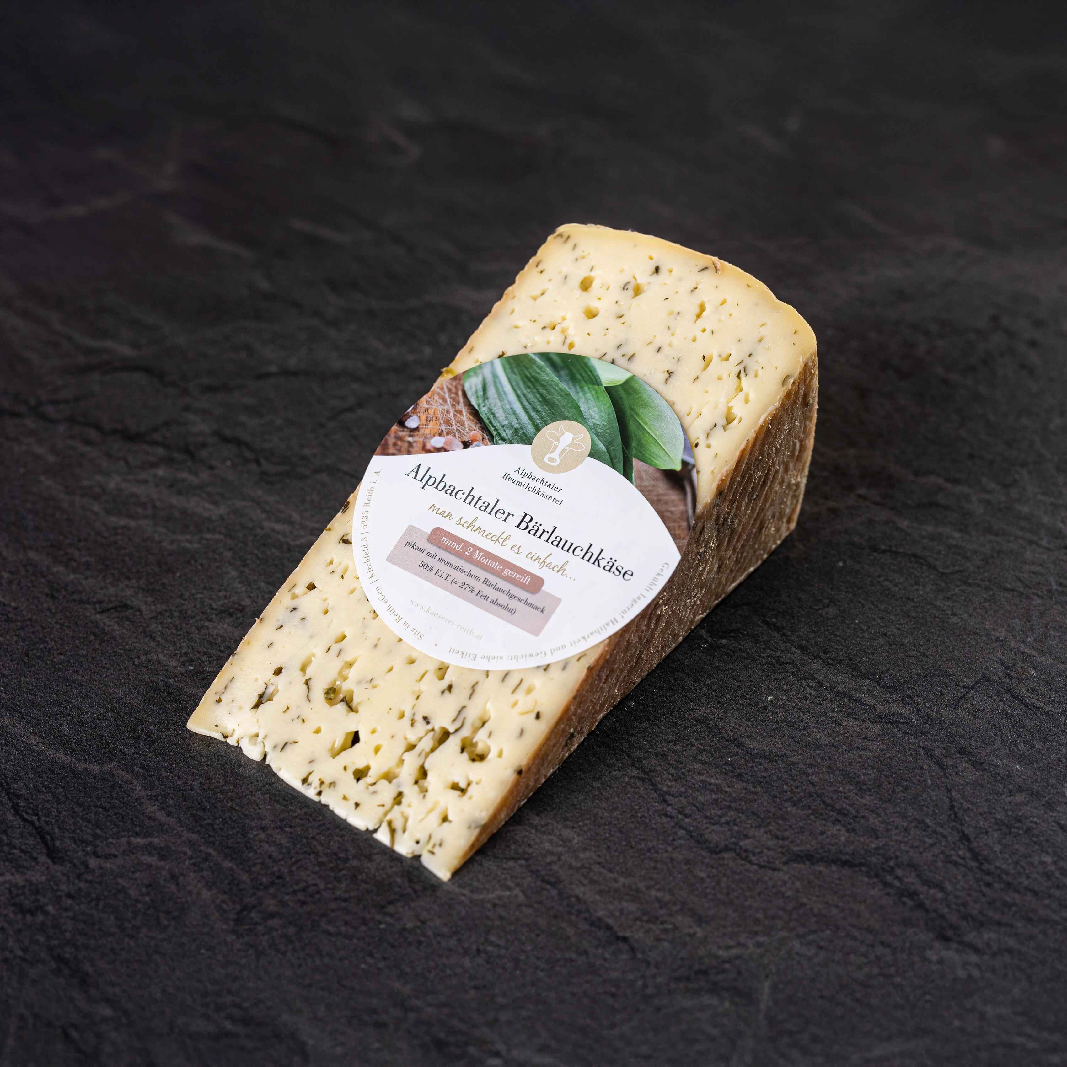 Alpbachtaler Bärlauchkäse Ein Stück Alpbachtaler Bärlauchkäse mit Etikett und Kräuterstückchen liegt auf dunklem Steinuntergrund.