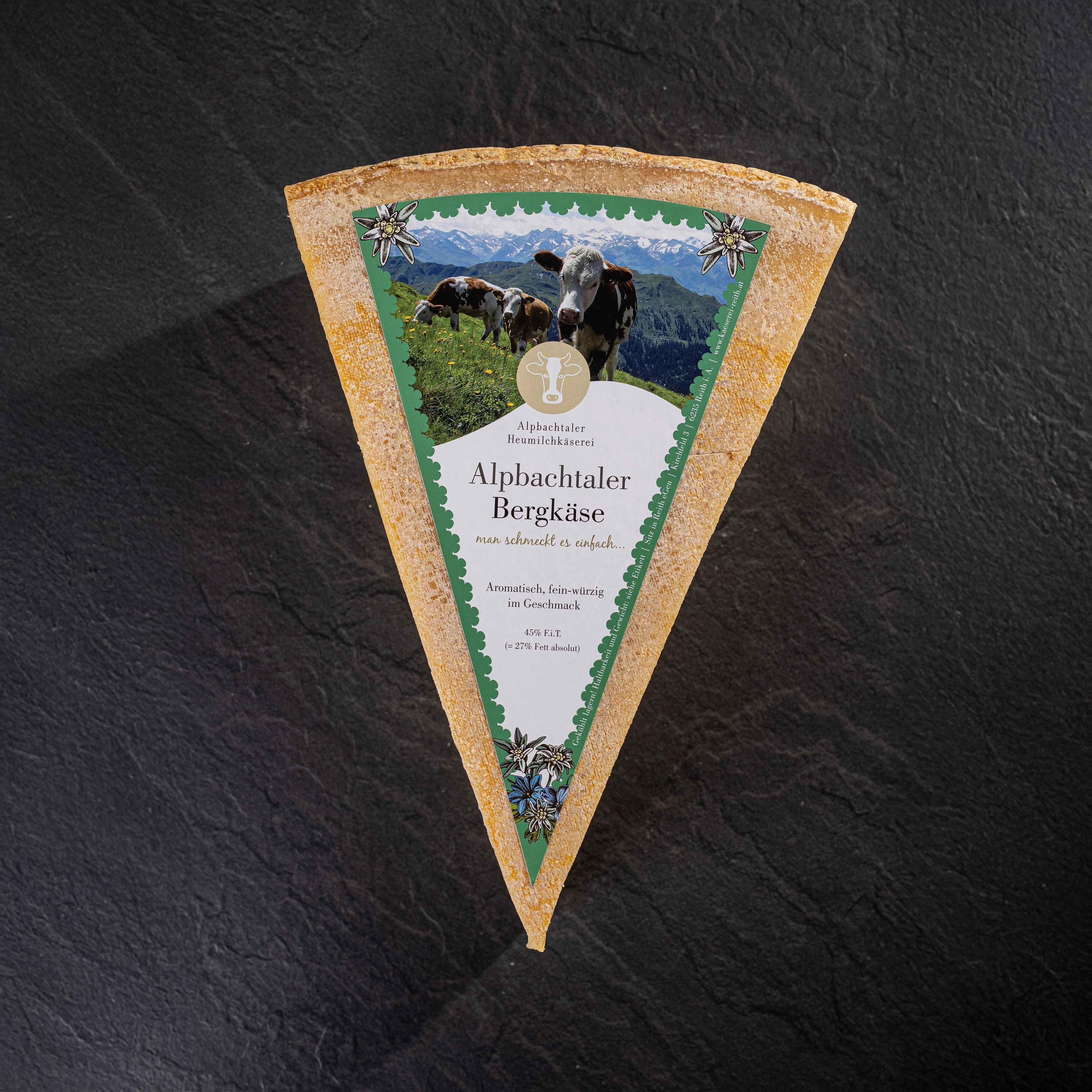 Ein Stück Alpbachtaler Bergkäse mit grünem Etikett liegt auf dunklem Steinuntergrund.