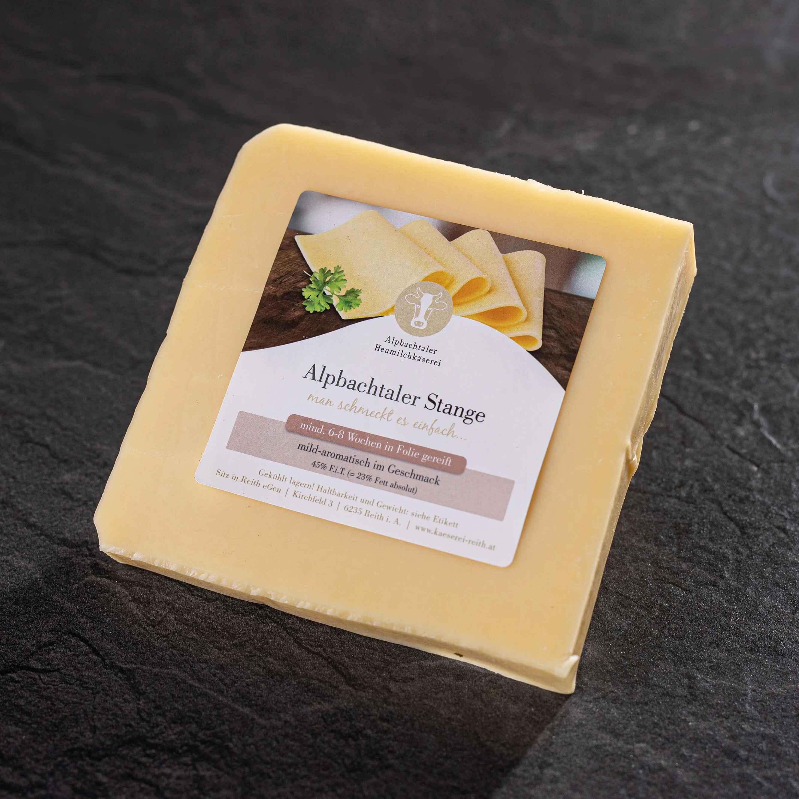 Ein Stück Alpbachtaler Stange-Käse mit Etikett liegt auf dunklem Steinuntergrund.