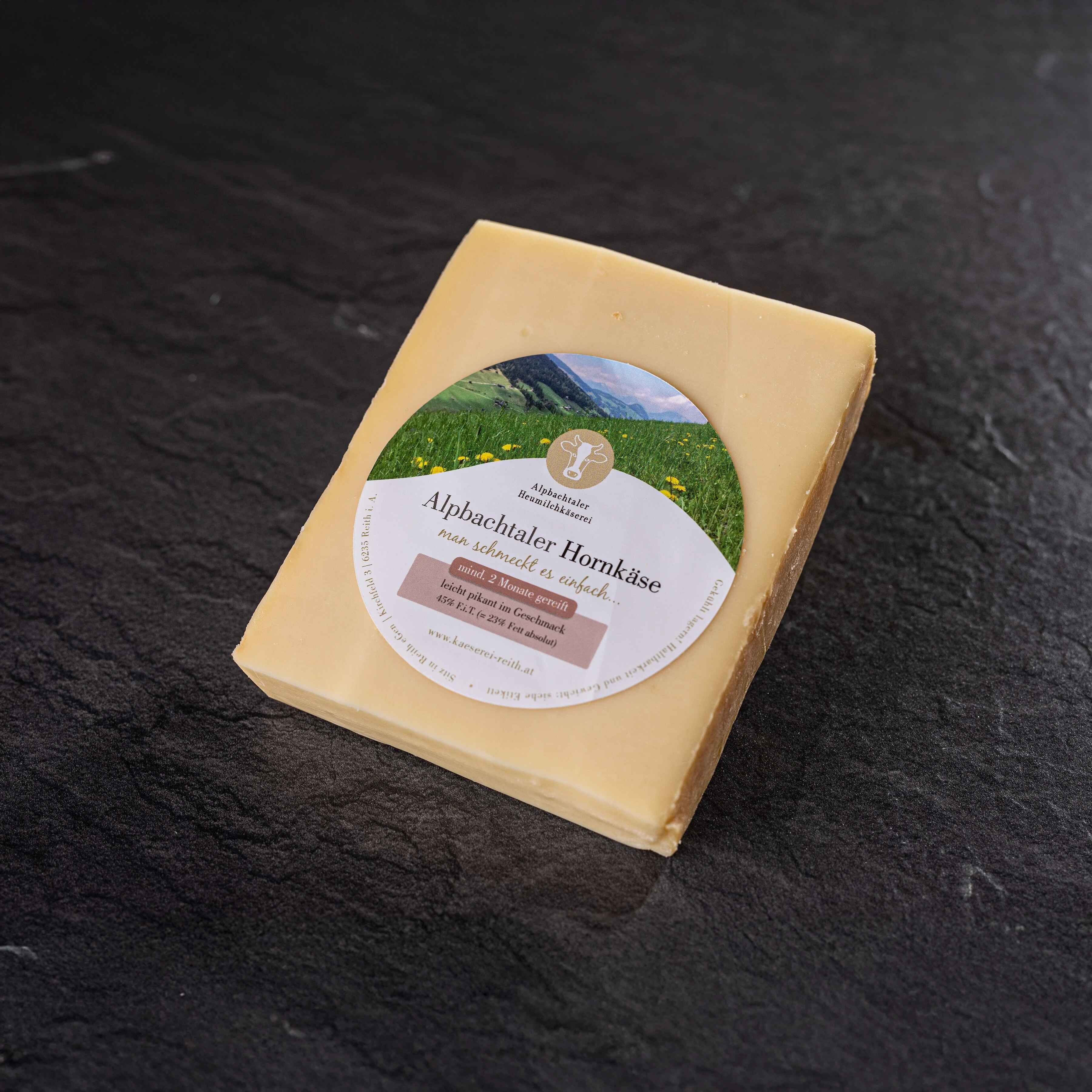 Ein Stück Alpbachtaler Hornkäse mit Etikett liegt auf dunklem Steinuntergrund.