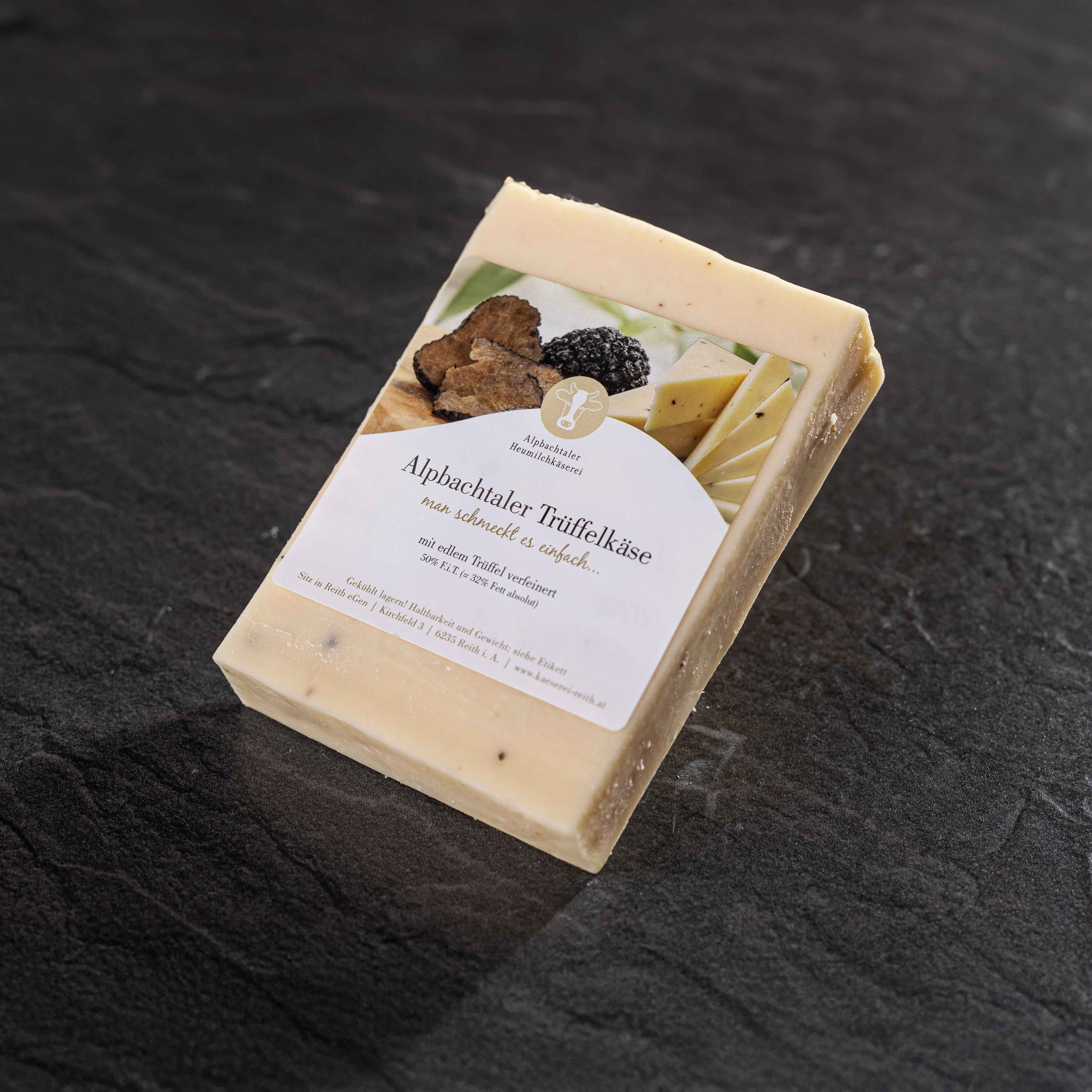 Ein Stück Alpbachtaler Trüffelkäse mit Etikett liegt auf dunklem Steinuntergrund.